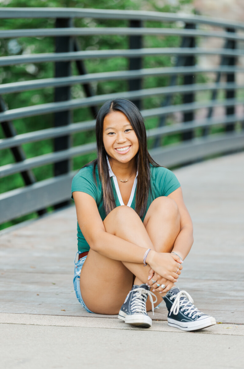 girl smiling at the camera and sitting on a bridge at sharon mills park in manchester