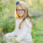 Michigan family photographer shows a Girl smiling at the camera and sitting in a field of tall grasses near Ann Arbor Michigan
