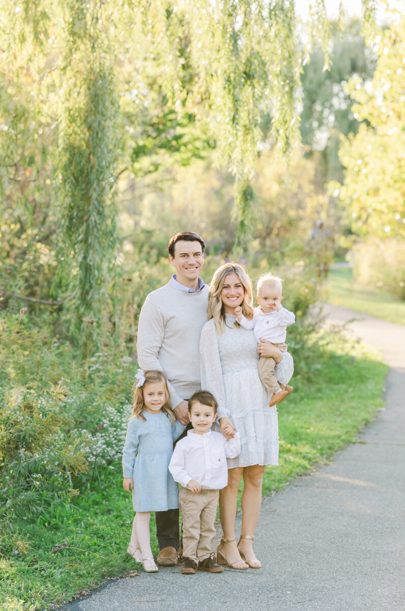 Family of five standing on a paved path in the trees and smiling at the camera