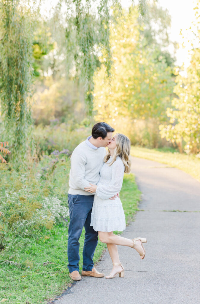 Top 5 Ann Arbor Photo Locations: Couple kissing on a path near a weeping tree at Lillie Park in Ann Arbor.