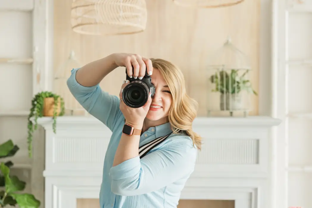 Stacy Anderson Photography shows a woman sitting at a desk smiling down at the computer with camera and flowers close by. In a studio near Ann Arbor Michigan.